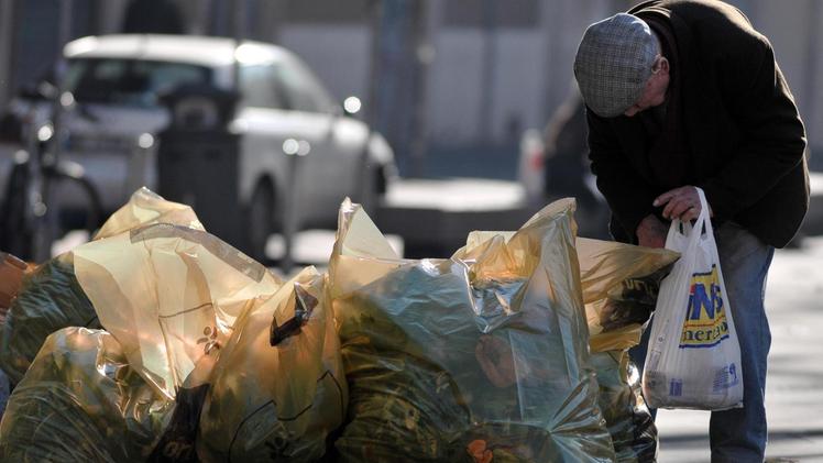 Un anziano cerca qualcosa fra i rifiuti, una scena emblematica dell’aumento delle condizioni di povertà